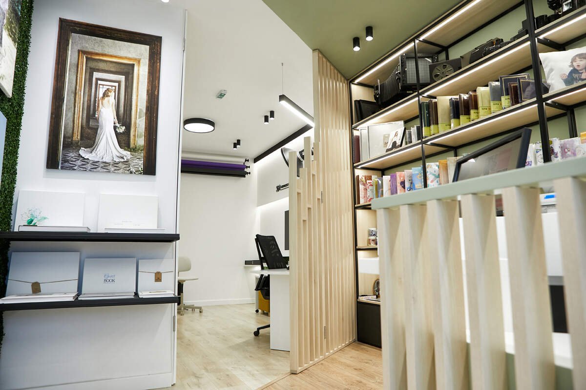 A modern, neatly organized office with a bookshelf filled with books, electronic devices, and framed pictures. There is a large painting of a woman in a white dress on the wall, and the space features wooden accents and lighting.