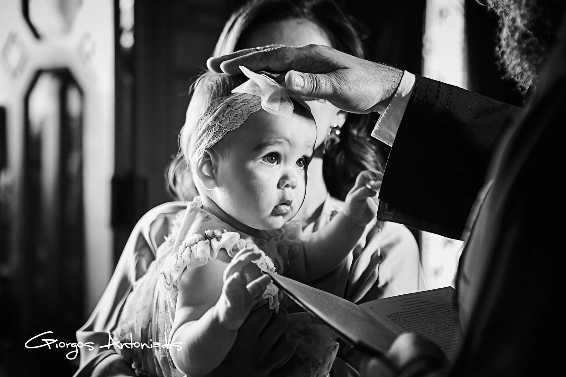 A young girl being blessed or anointed by a man in a formal setting, with the girl holding a book and looking attentive.