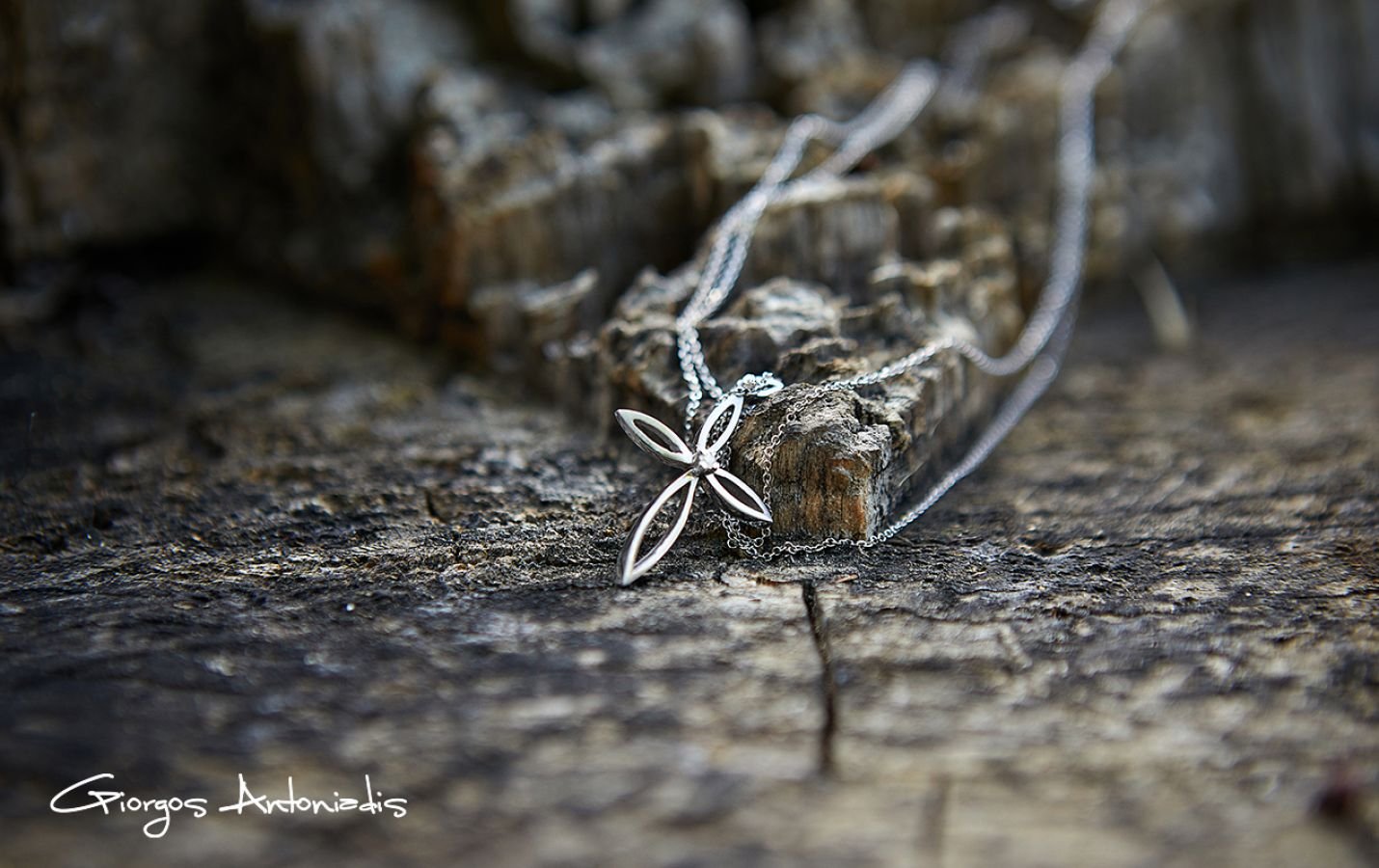 Silver necklace with a flower-shaped pendant resting on a rough wooden surface with a small piece of wood in the background.