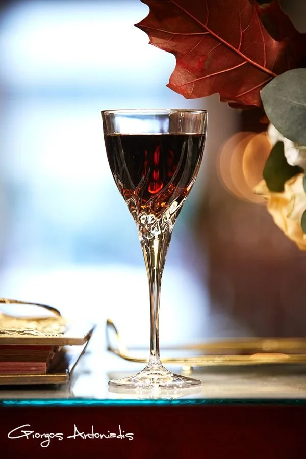 A glass of red wine on a table with leaves and books nearby.