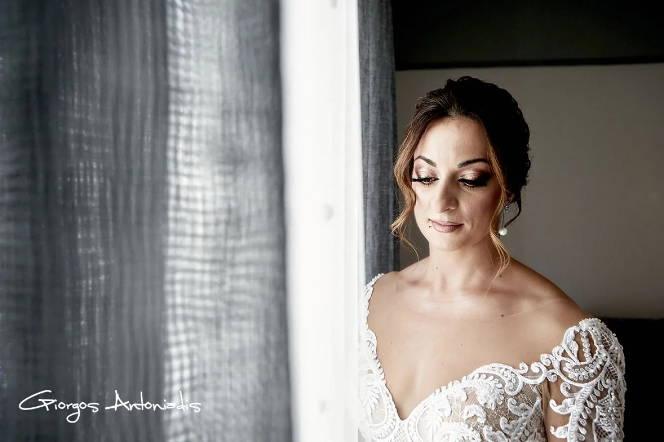 A bride in a white lace wedding dress looking out a window.