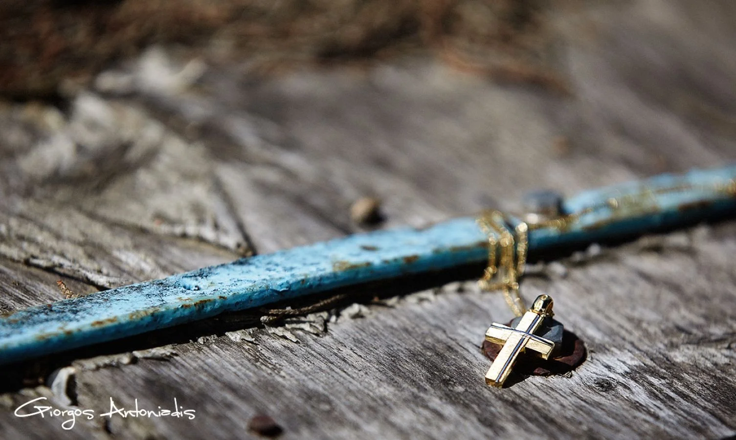 A gold cross necklace and a blue bracelet with gold beads are lying on a weathered wooden surface.