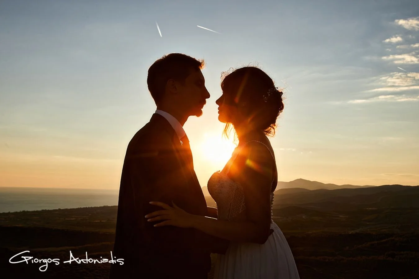 A silhouette of a couple, a man and woman, facing each other during sunset outdoors with a scenic landscape and ocean in the background.