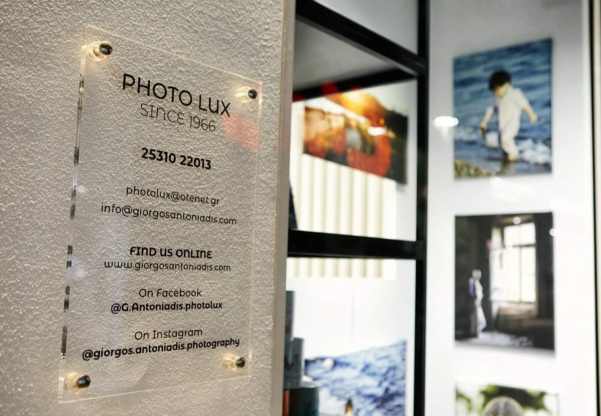 Photographer's contact info on a transparent signboard in front of a wall displaying landscape photographs.