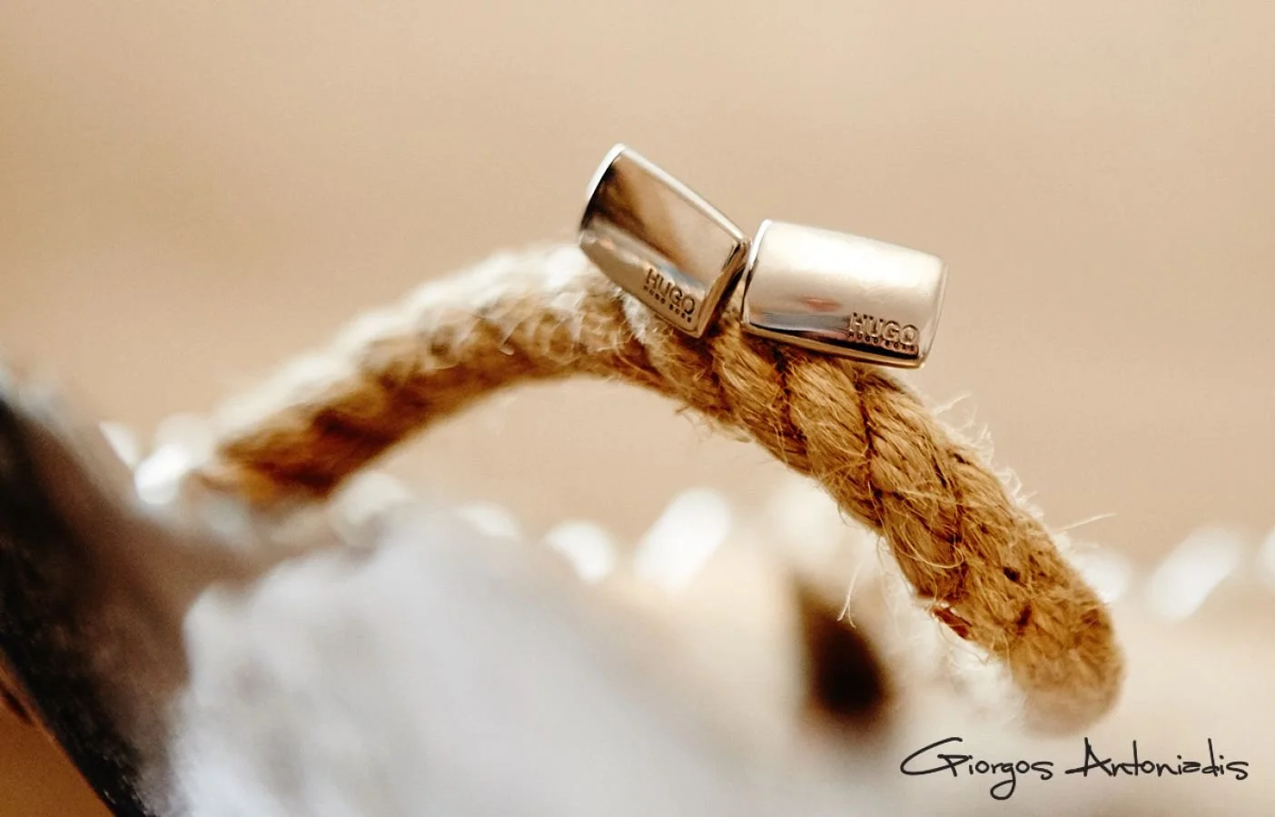 Close-up of a small rope with two silver hoop earrings resting on top, with a blurred background and a signature reading 'Giorgos Antoniadis'.