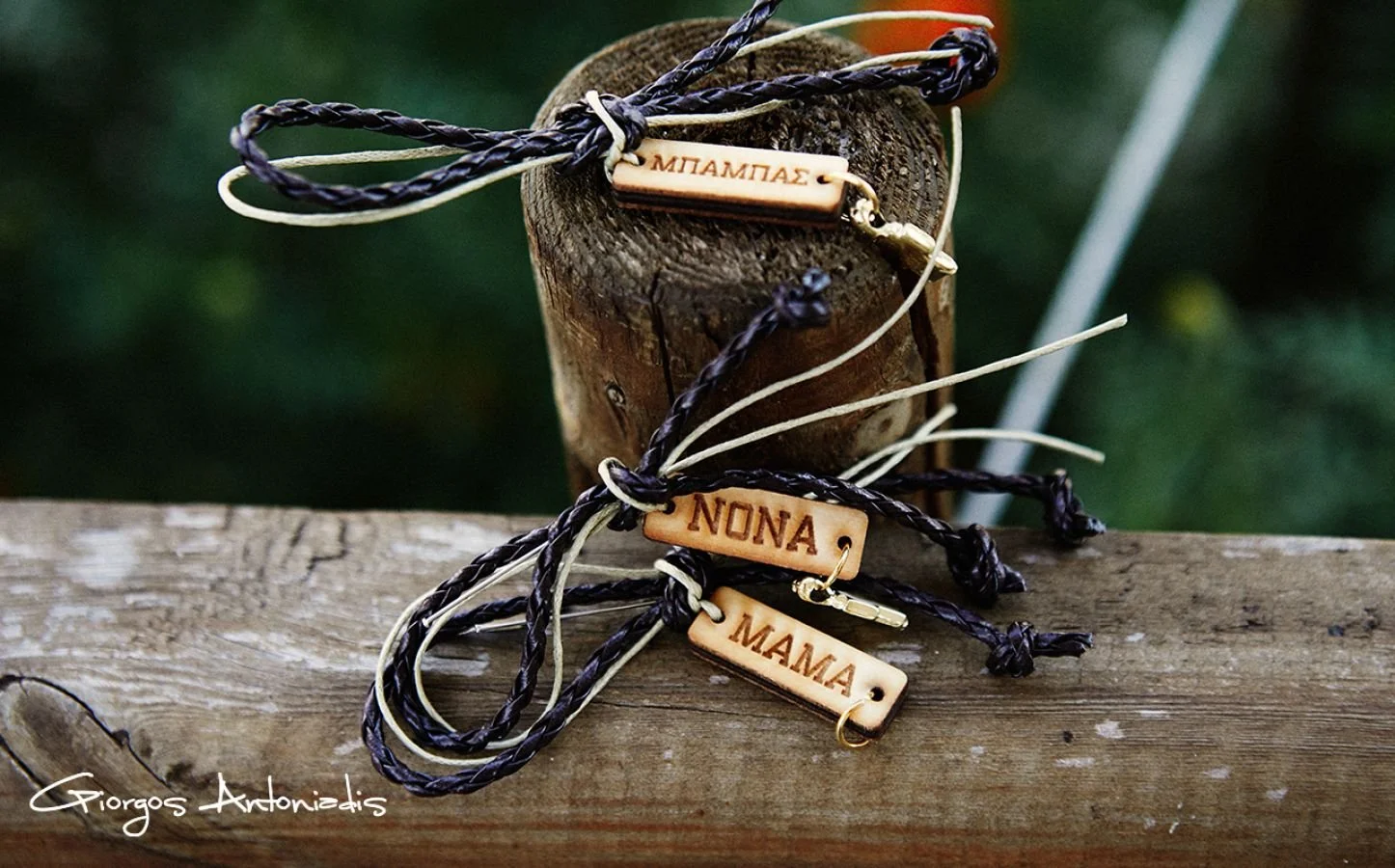 Three bracelets with personalized wooden tags in Greek and English, resting on a wooden surface with a rustic background.