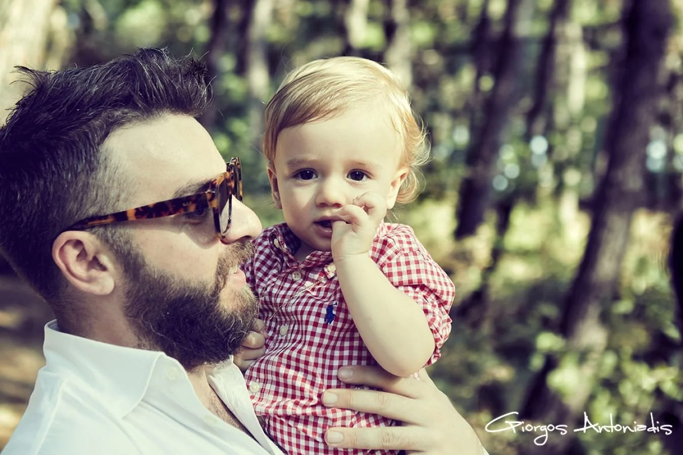 A man with brown hair, a beard, and glasses holding a young girl with blonde hair in a forest setting.