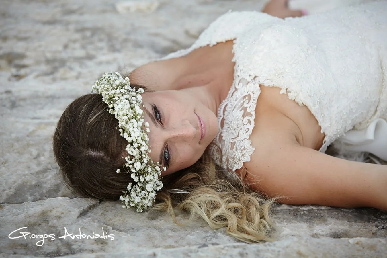 A woman lying on the ground wearing a white lace wedding dress and a flower crown made of baby's breath flowers.