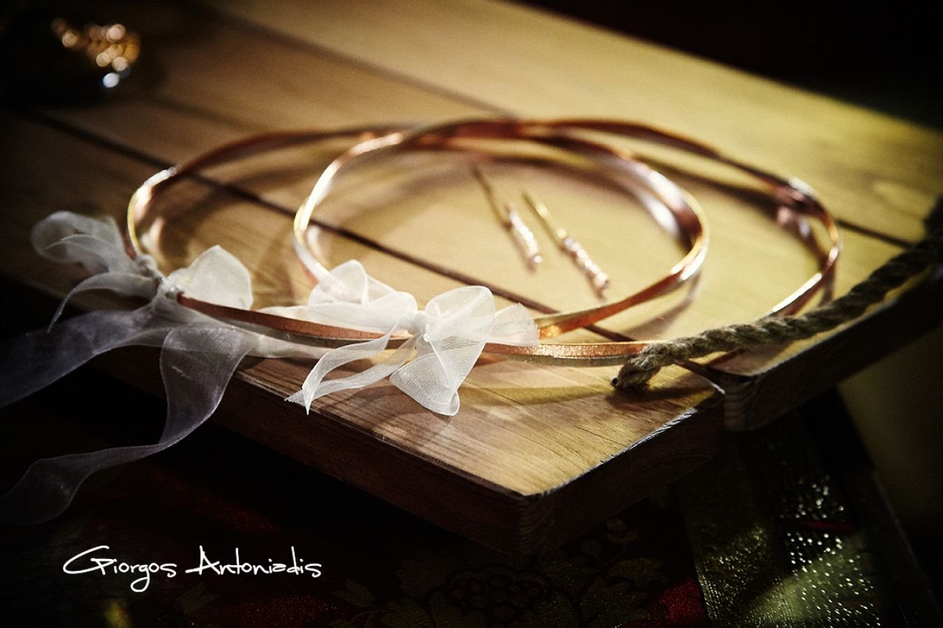 A pair of gold wedding jewelry, including a necklace and earrings, placed on a wooden surface with soft lighting and a decorative ribbon.