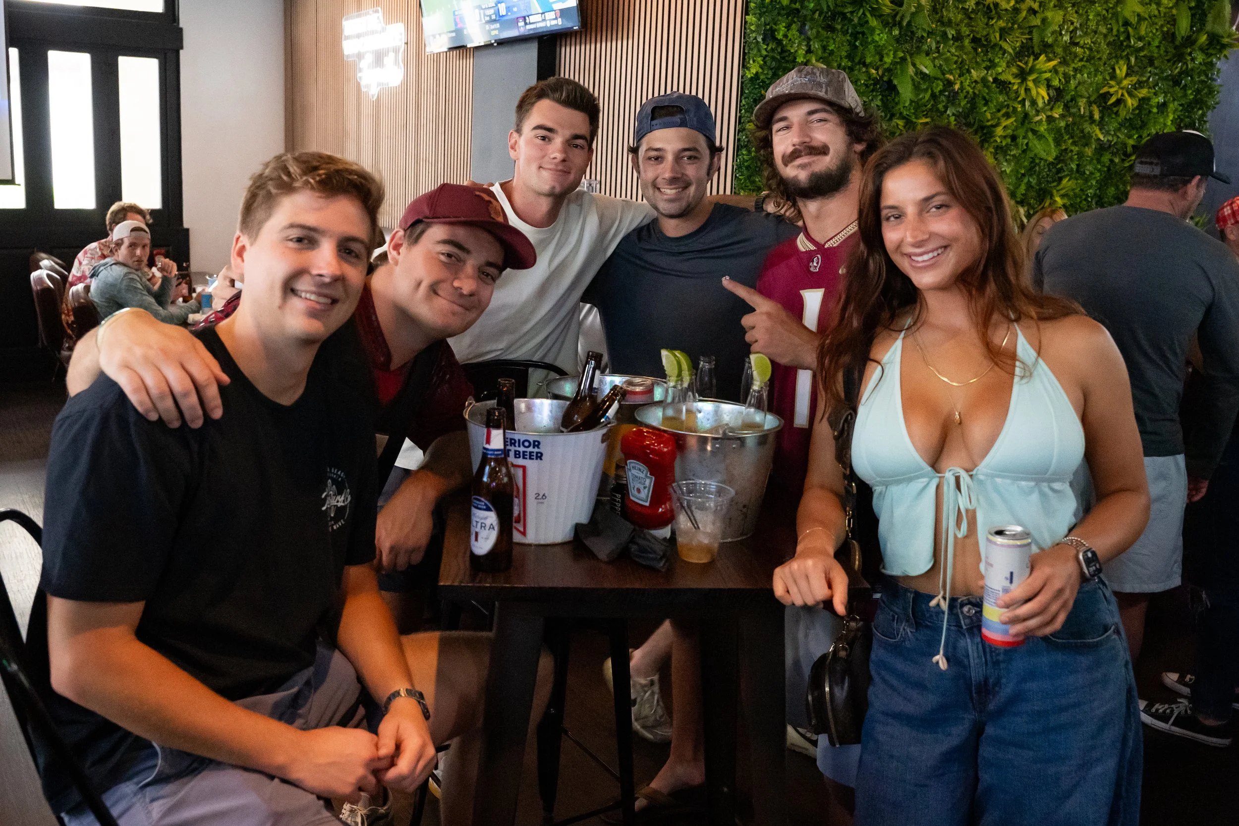 Group of six friends smiling and standing around a table with drinks at Nieko's Neighborhood Bar and restaurant joining us for saturday football watch parties