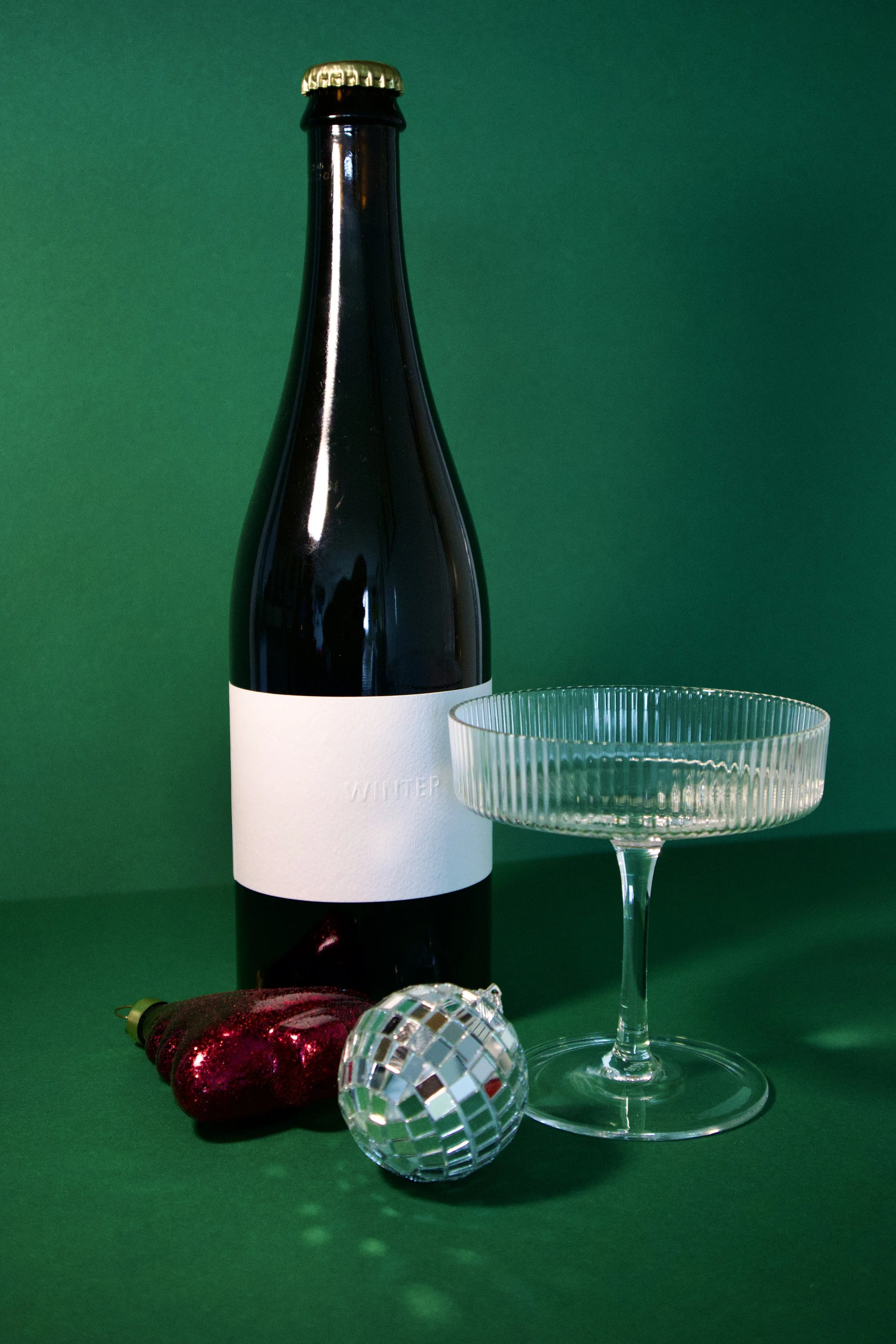 Een fles wijn, een cocktailglas, een kerstboord, en een disco bal op een groene achtergrond.