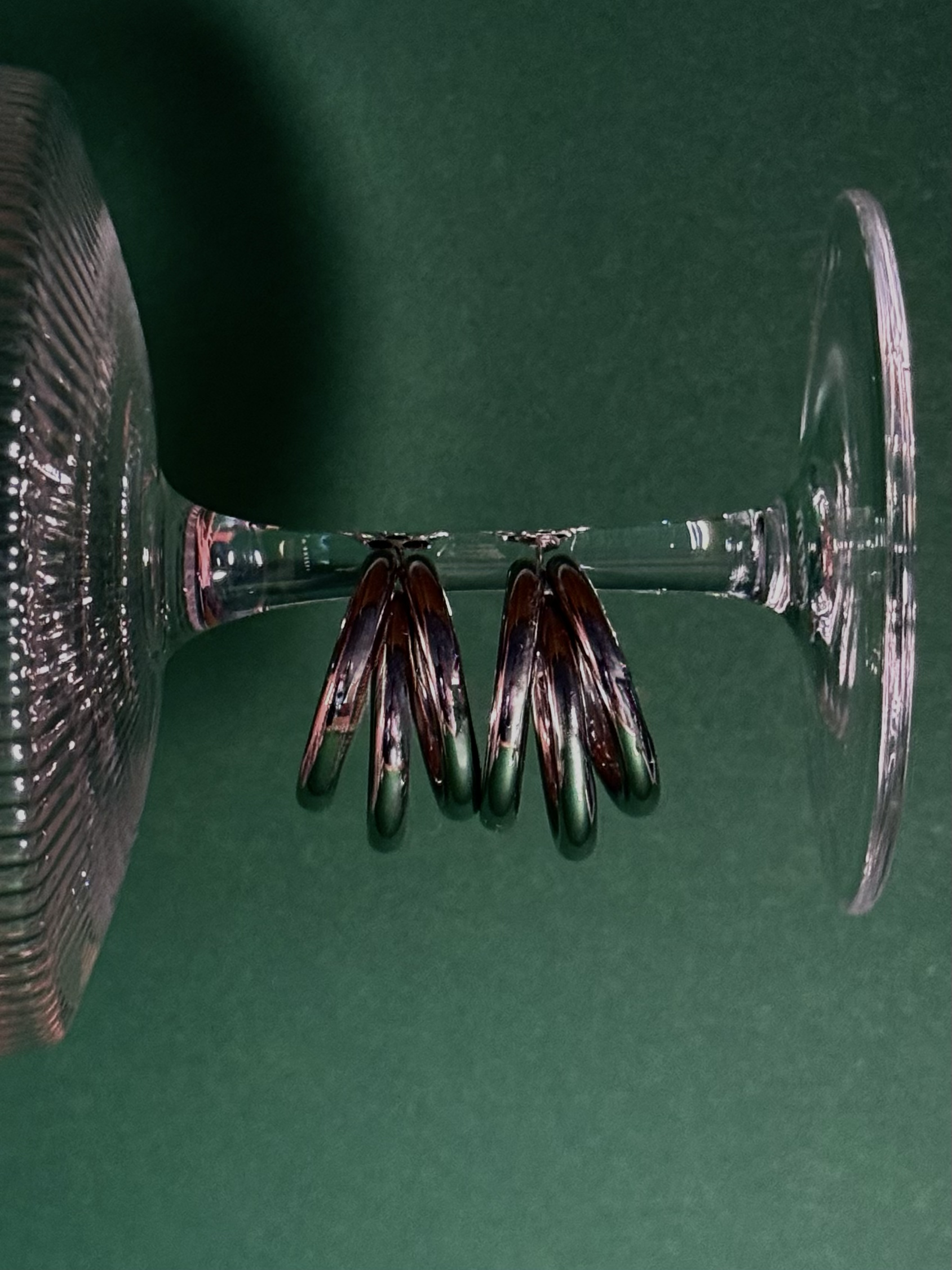 Een leeg, omgekeerd wijnglas met meerdere nagellakpotloden onderaan, tegen een groene achtergrond.