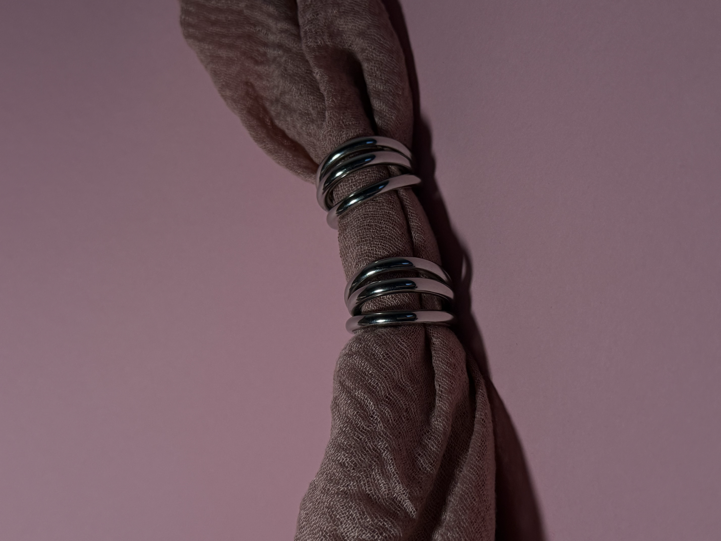 Een vinger met drie zilveren ringen, omwikkeld met een lichtbruine stoffen handschoen, tegen een roze achtergrond.