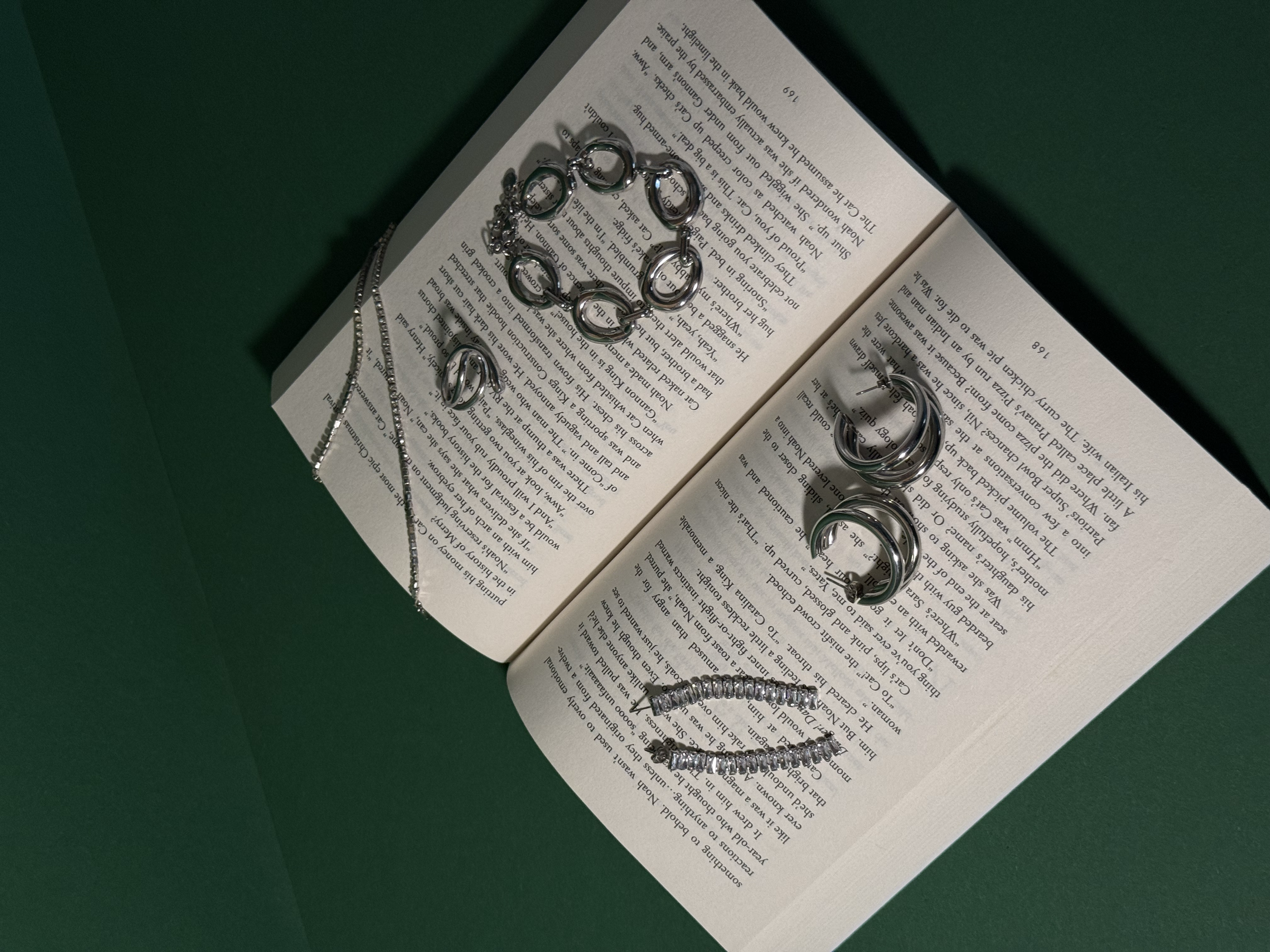 Een open boek met verschillende zilveren sieraden, waaronder kettingen, kettingen, oorbellen, en een armband, uitgestald op de pagina's.