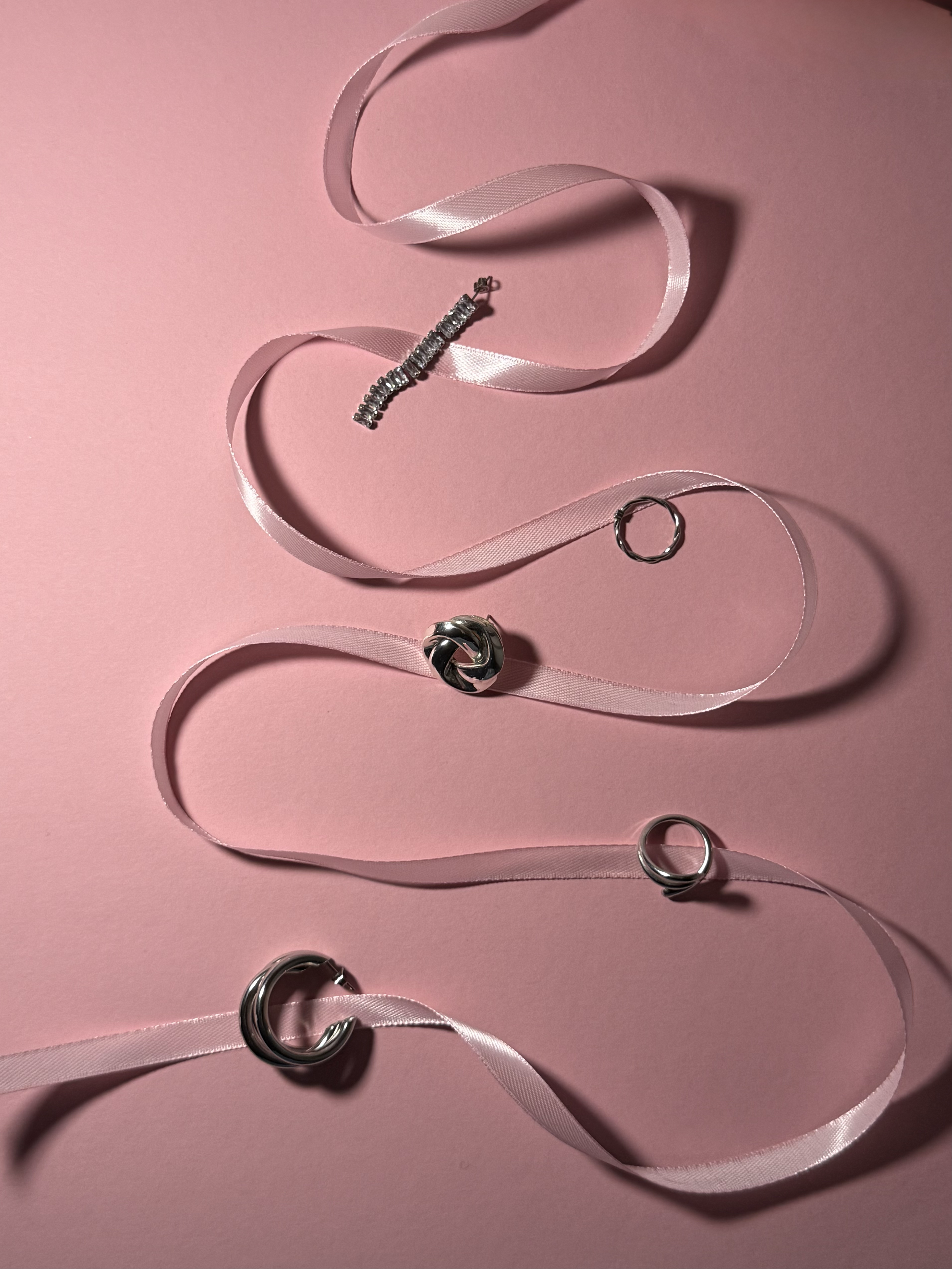 Verschillende zilveren ringen en een pink lint op een roze achtergrond.