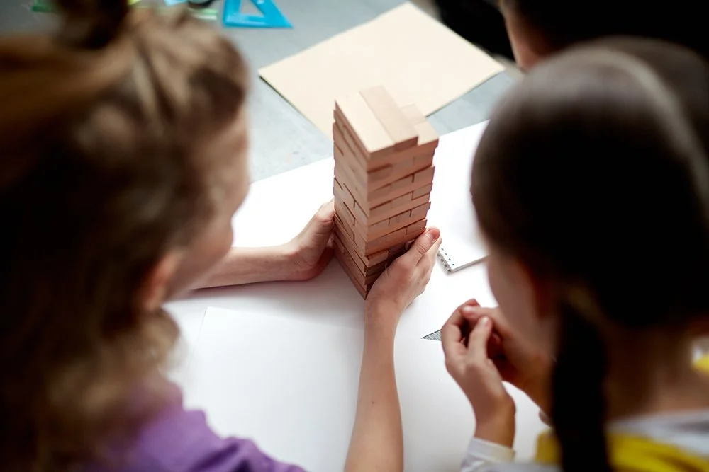 Three people examining a tower of red bricks on a desk.