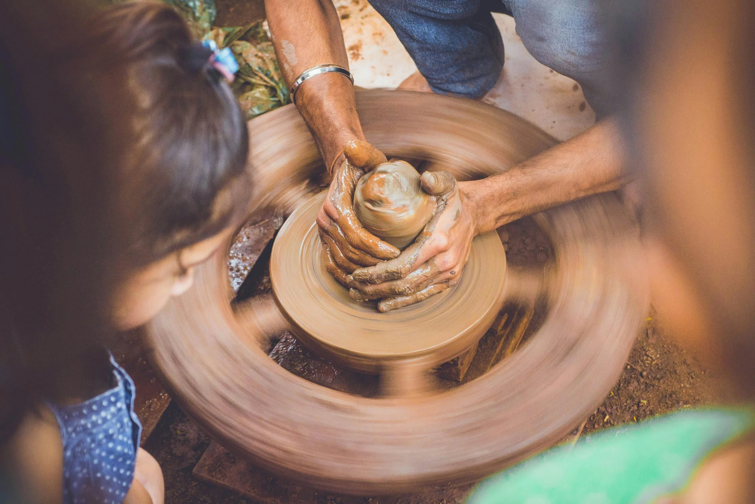 People working on a pottery wheel shaping clay into a pot.