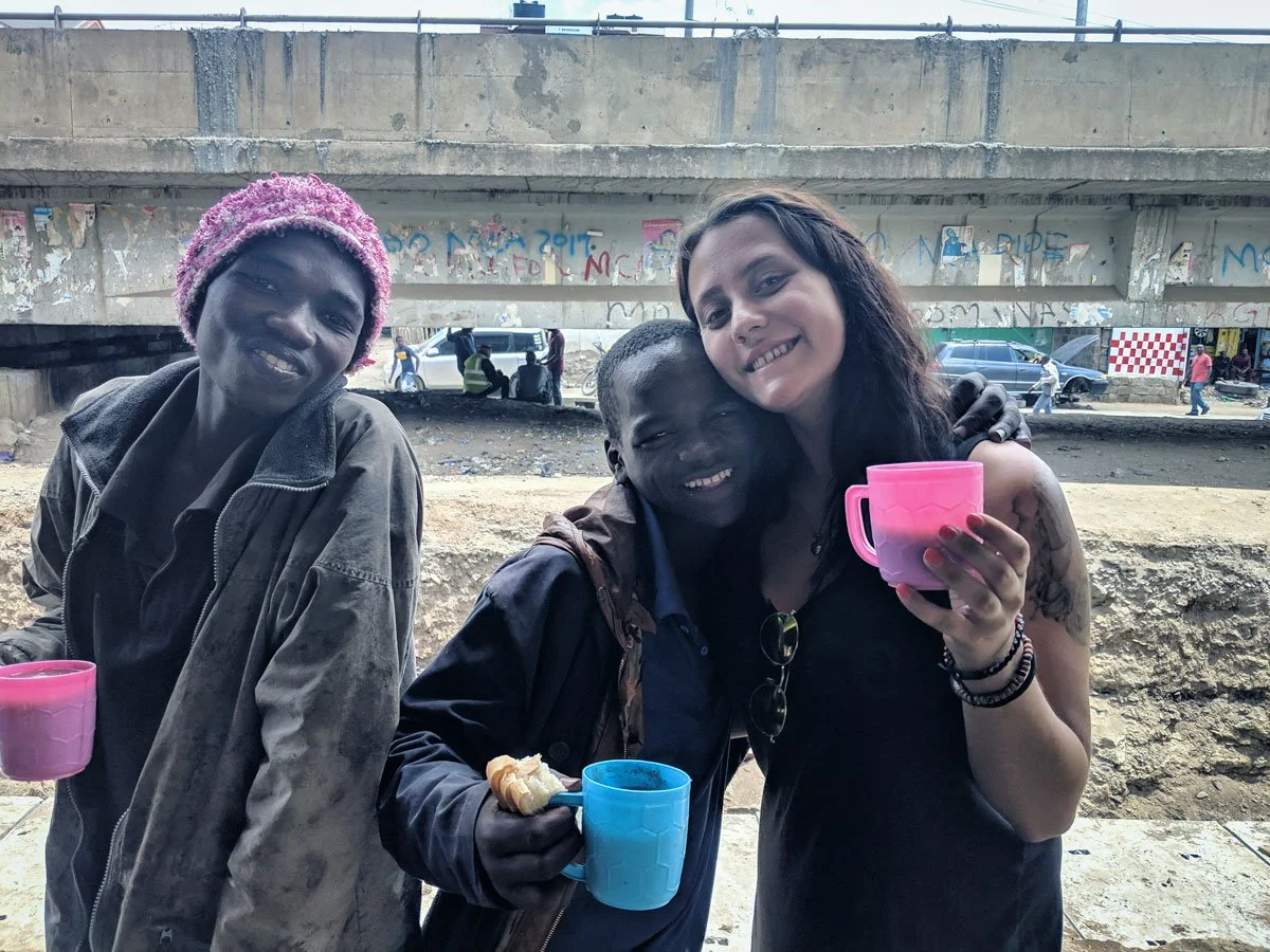 Nathalie Narbel mit zwei Strassenkinder von Nairobi welchen sie Essen zubereitet hat. Alle lachen glücklich.