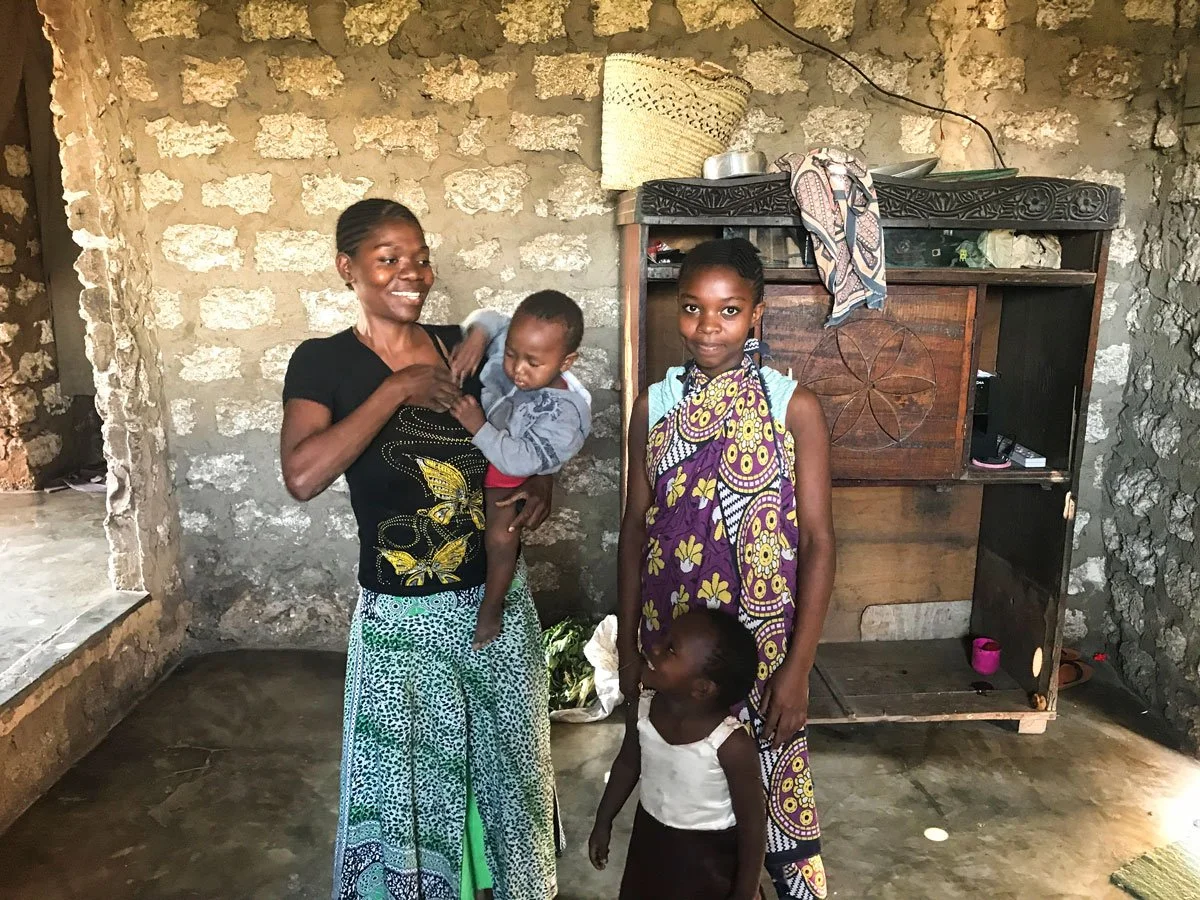 Eine afrikanische Mutter steht mit ihrer jugendlichen Tochter und den zwei kleinen Mädchen glücklich in ihrem Haus welches durch die Hilfsorganisation Nafrika erbaut wurde.