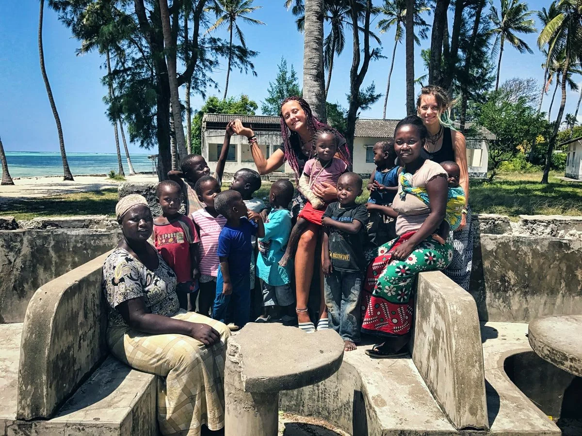 Zwei weisse junge Frauen sitzen in einer Gruppe afrikanischer obdachloser Kinder, eines der Kinder trägt einen Gips, es wurde durch die Hilfsorganisation Nafrika medizinisch versorgt