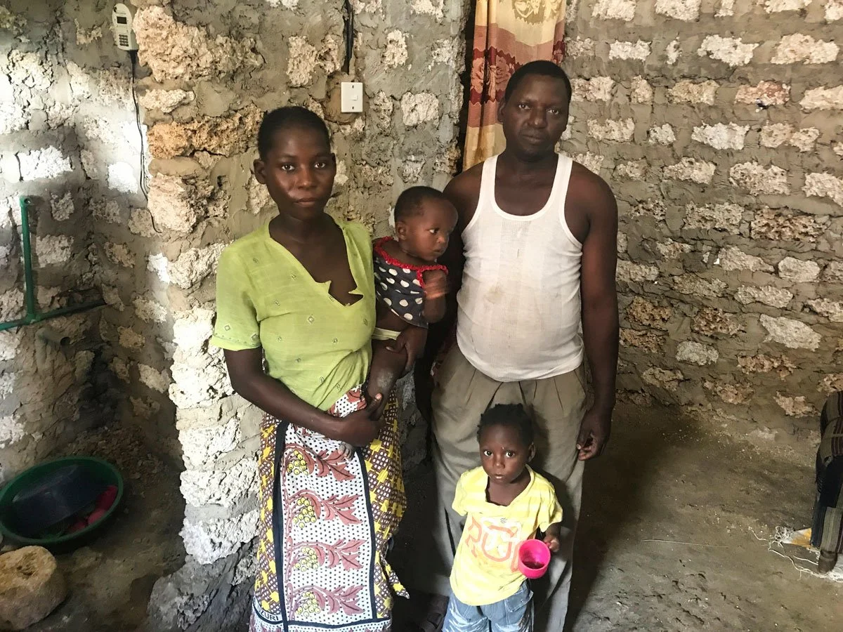 Eine junge afrikanische Familie steht in ihrem Wohnraum welcher von Nafrika gebaut wurde. Man sieht den Eltern an dass sie schwierige Zeiten hinter sich haben.