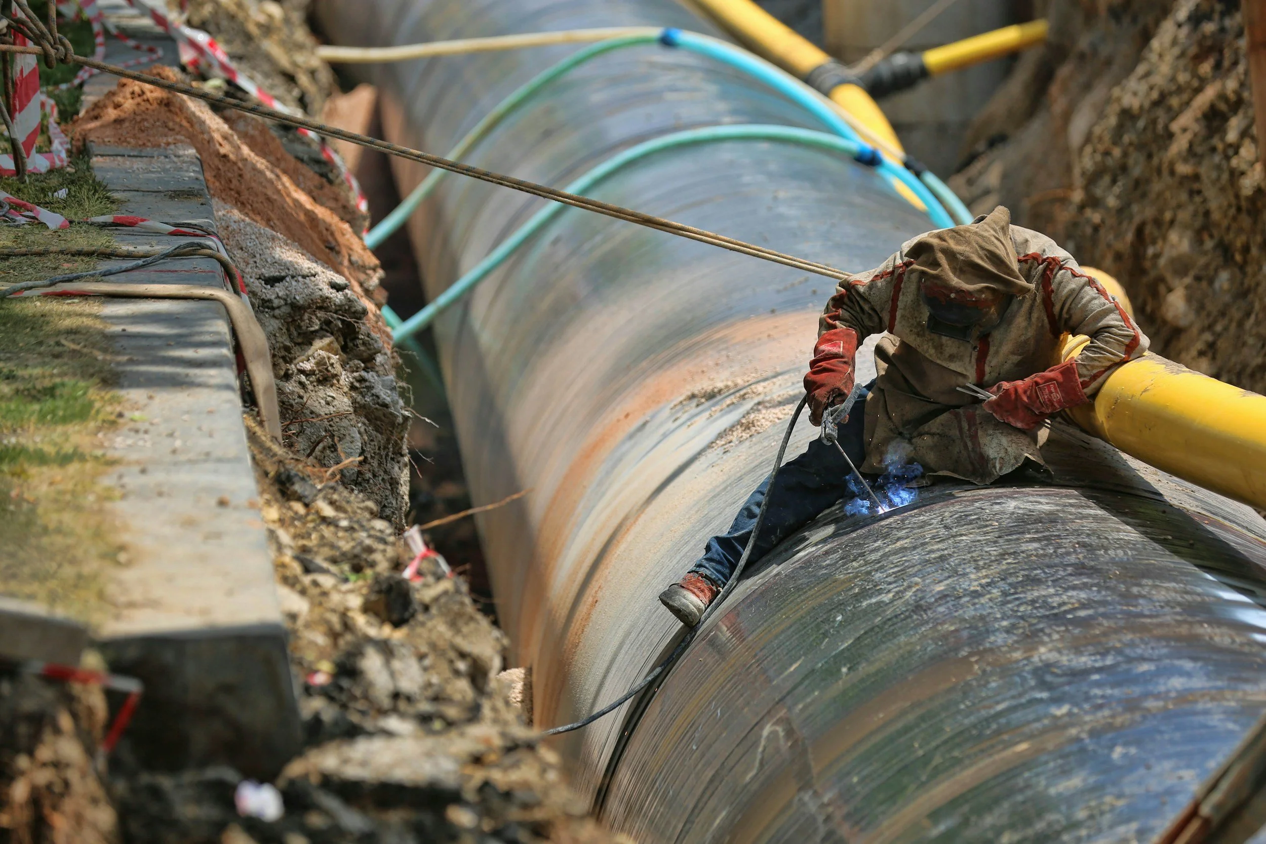 Worker performing maintenance on a large buried pipeline, representing hands-on intervention and operational planning in the field.