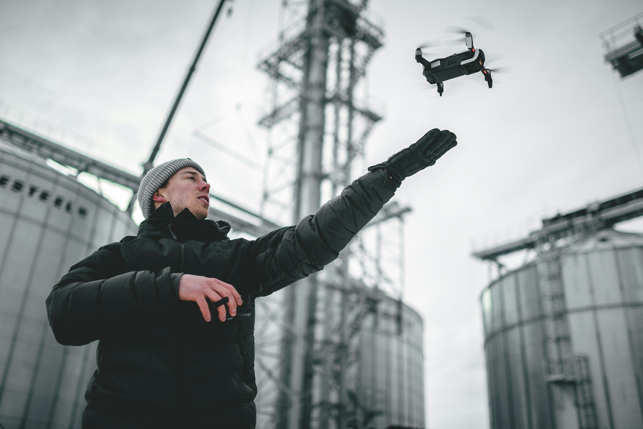 Field operator gesturing toward industrial infrastructure while a drone flies overhead, representing aerial intelligence and sensing.