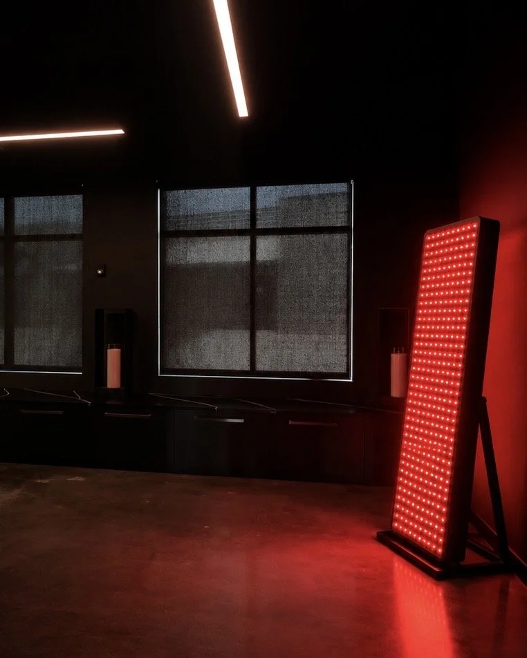 An interior room with black walls, a large red LED light panel, and three windows with black blinds.