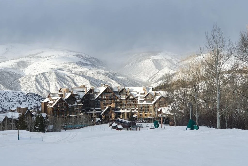 A snowy mountain landscape featuring a large multi-story chalet-style building surrounded by snow-covered trees and mountains.