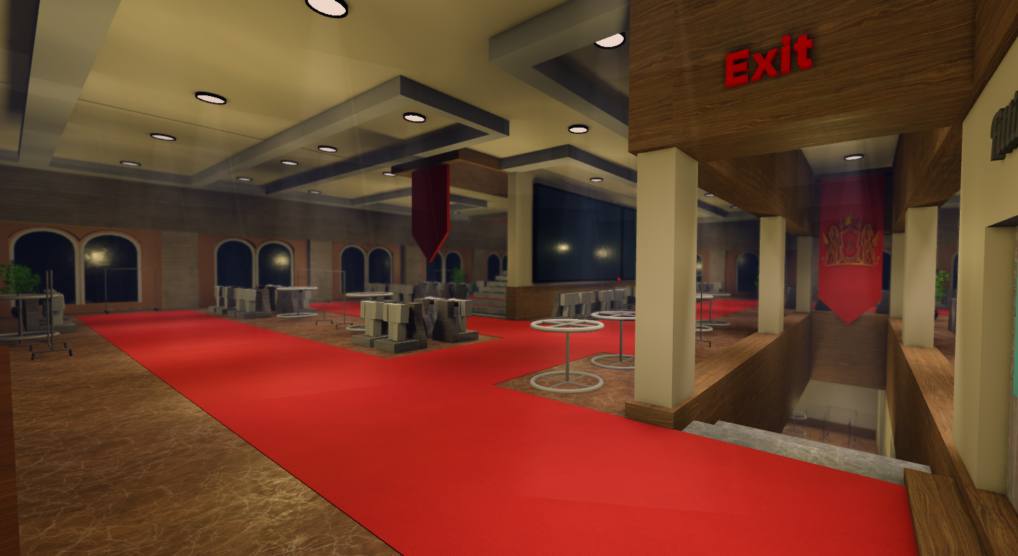 Interior of a building with a red carpeted hallway, tables, chairs, and a staircase leading down. An exit sign is visible on a wooden wall, and decorative banners hang from the ceiling.