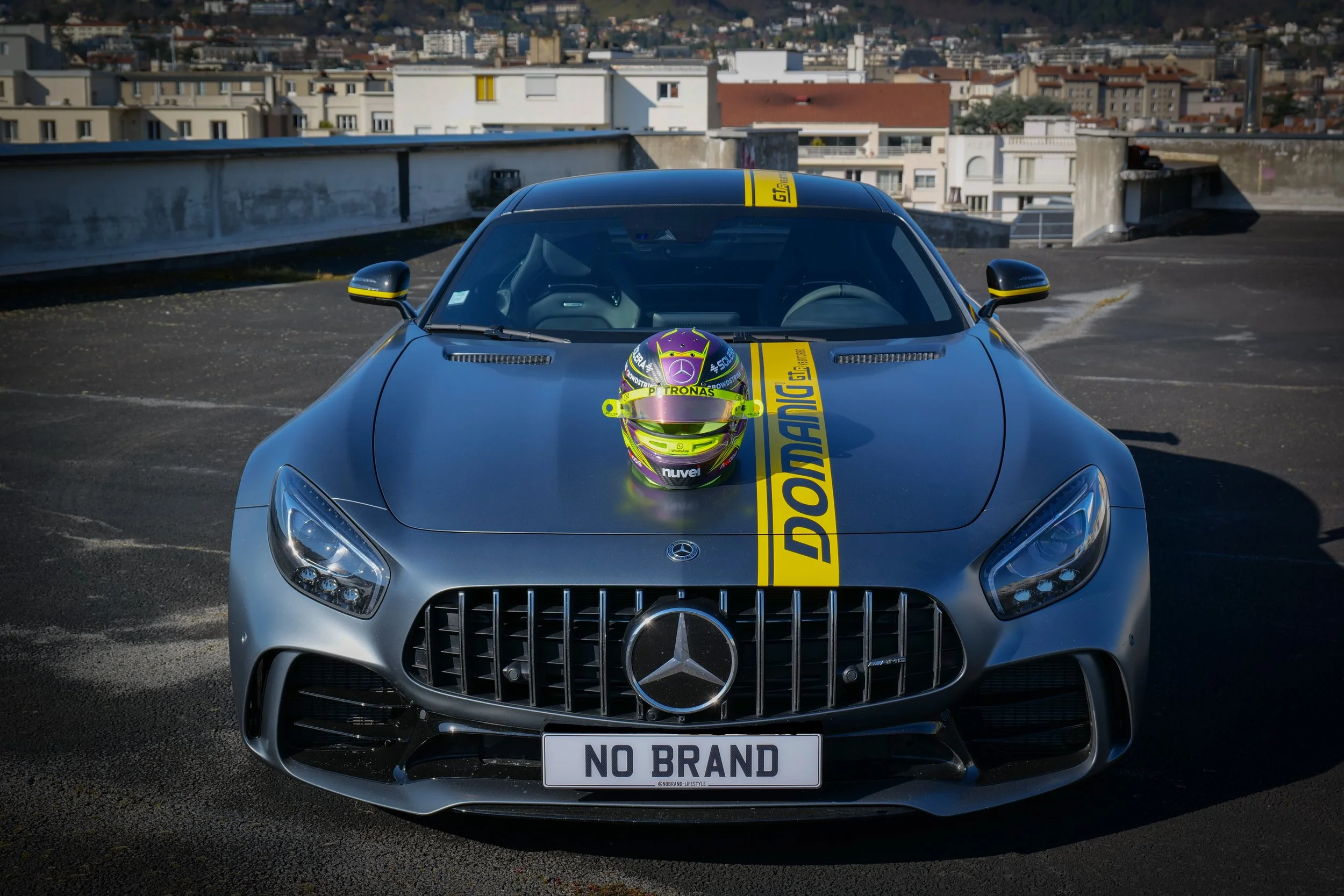 Voiture de sport Mercedes-Benz grise avec un casque de course violet et vert sur le capot et une bannière jaune avec écrit 'DORANG'.