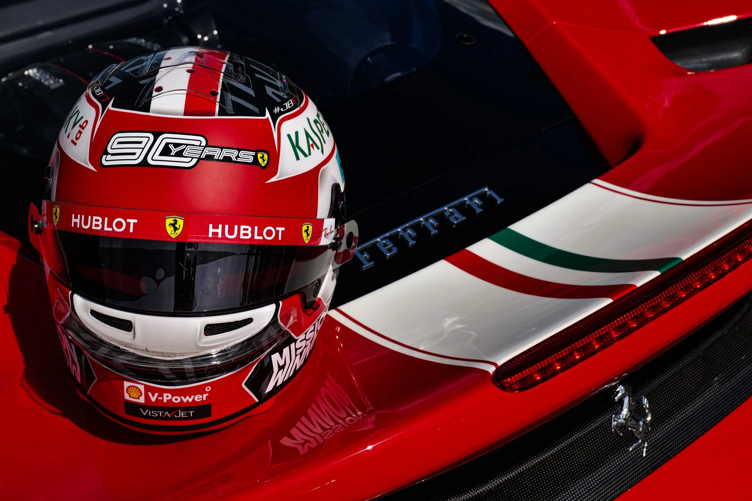 Casque de pilotage Ferrari avec logos de sponsor et le texte '90 Years' sur un fond rouge, blanc et noir.