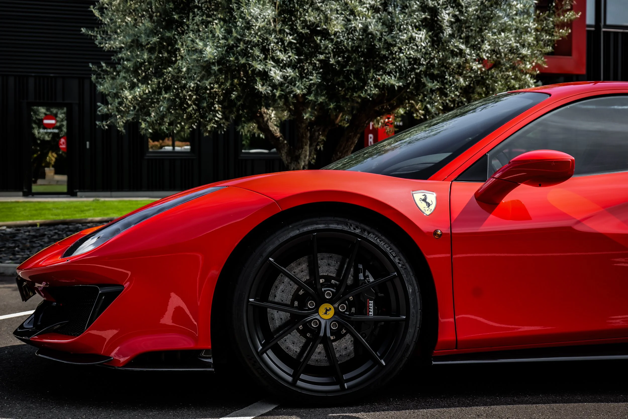 Voiture Ferrari rouge sportive, vue partielle de la roue avant et du capot, arrière-plan arbres et bâtiment