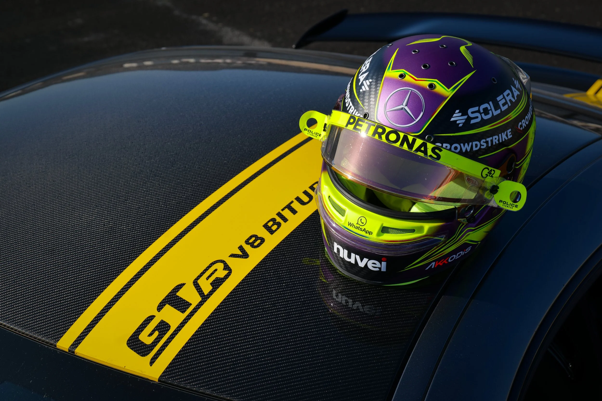 Casque de course sur la capote d'une voiture de course, avec marques et sponsors, couleurs violette, jaune et noir.