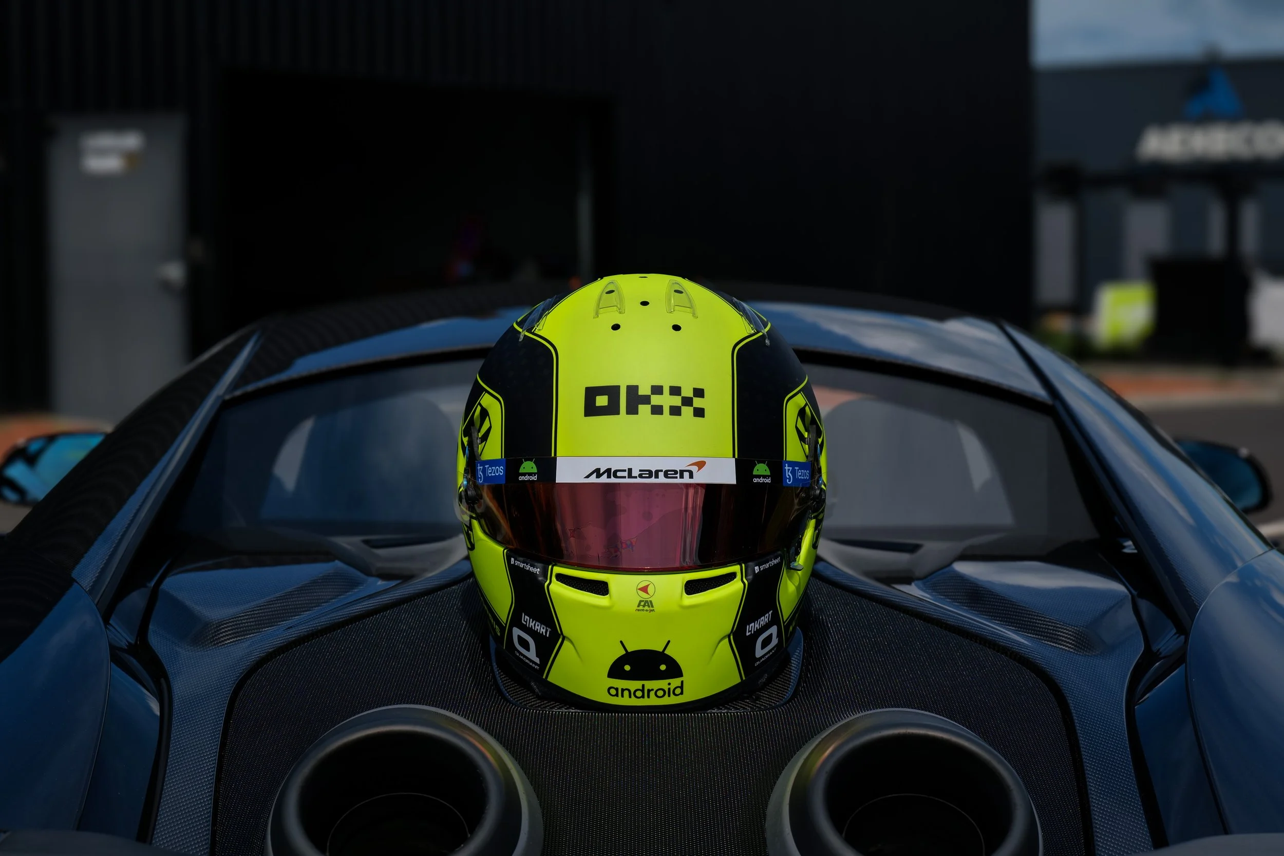 Casque de course jaune fluo avec visière sombre, posé sur une voiture de course en carbone.