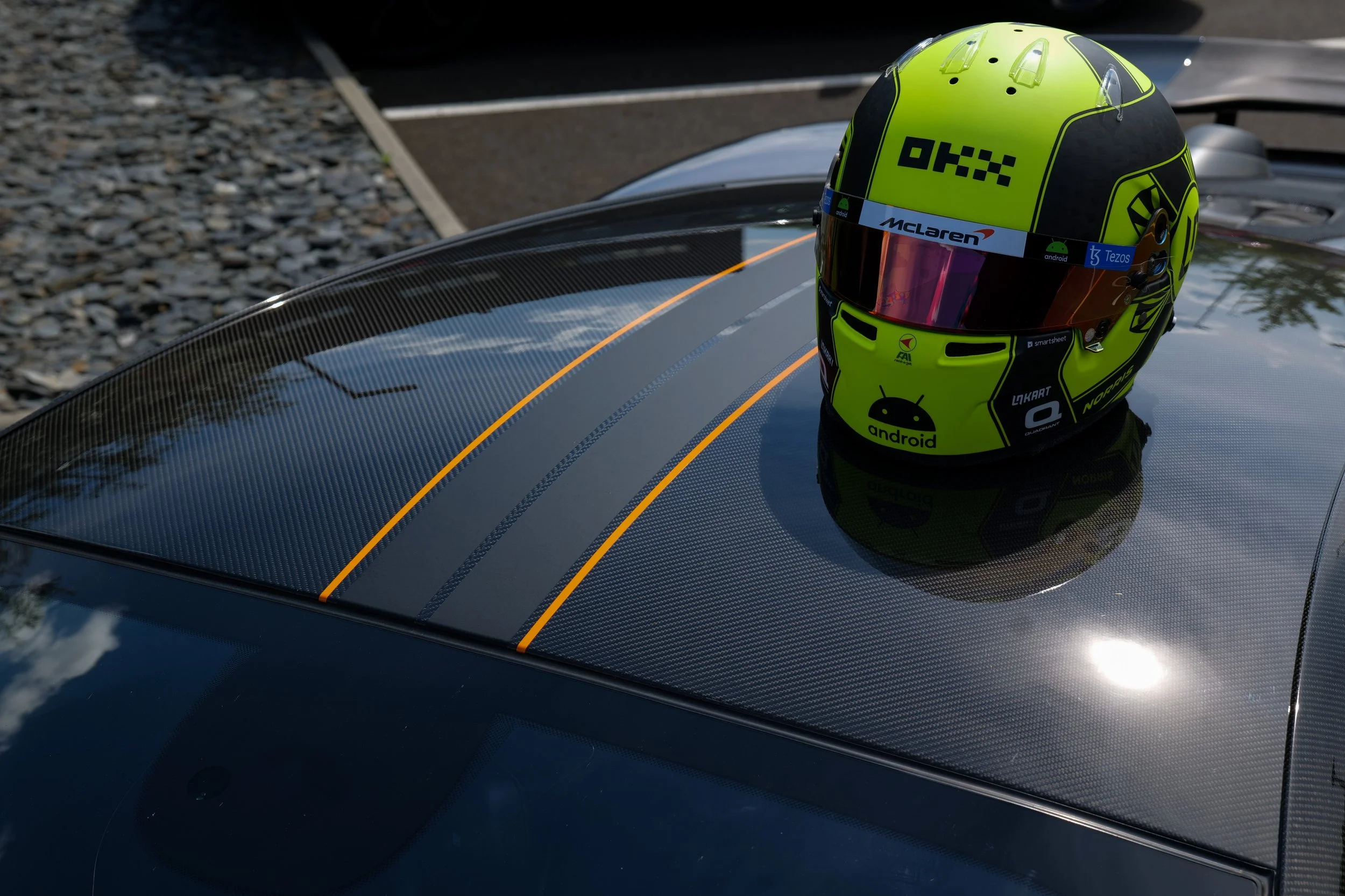 Casque de course jaune vif avec divers logos, posé sur le toit en fibre de carbone d'une voiture de course.