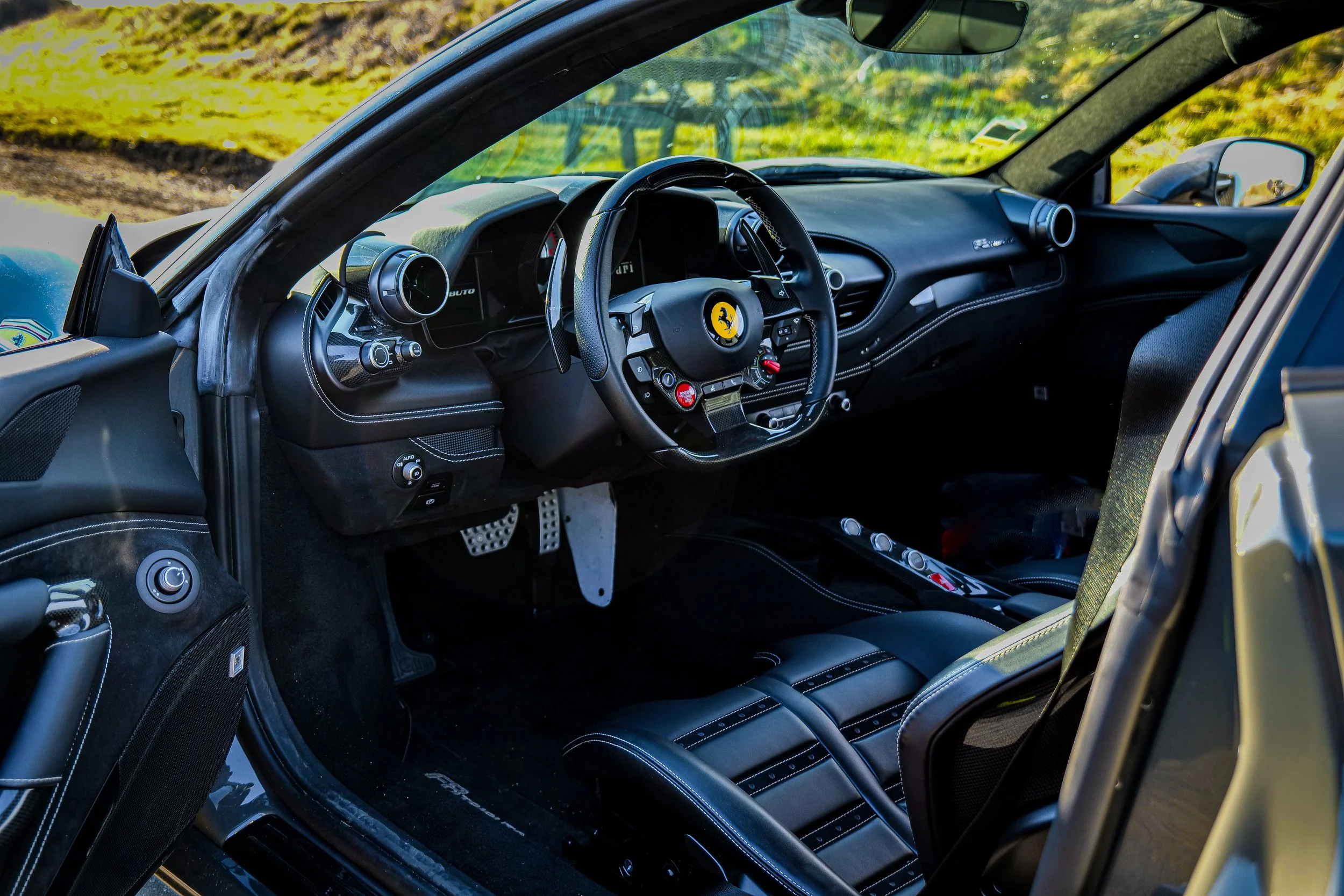 Intérieur d'une voiture de course Ferrari, vue du côté conducteur, avec un tableau de bord, un volant avec logo Ferrari, sièges en cuir noir et accoudoir.