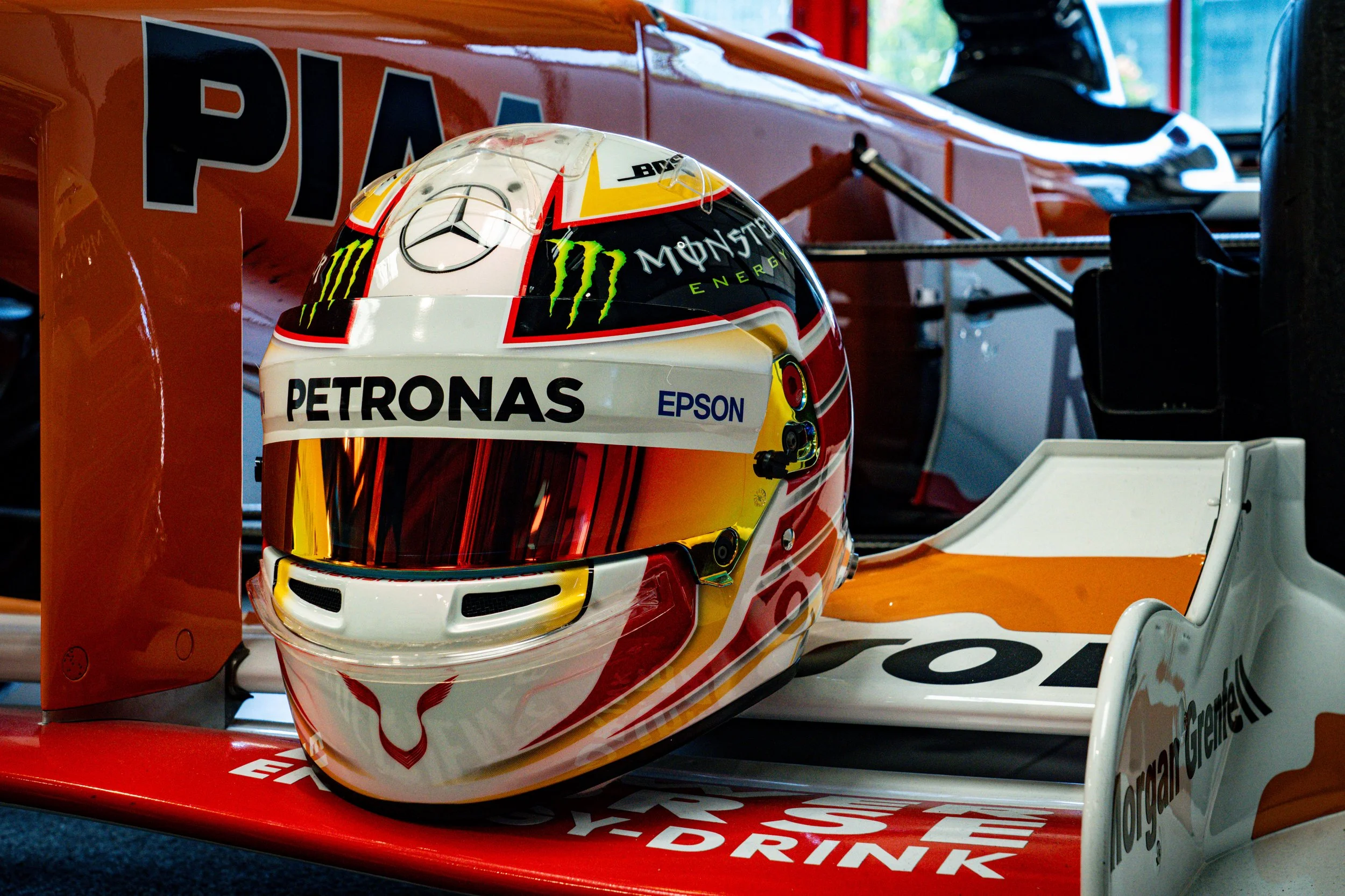 Casque de pilote de Formule 1 sur une voiture de course, avec logos PETRONAS, Monster Energy, Mercedes, et autres sponsors, dans une zone de garage.