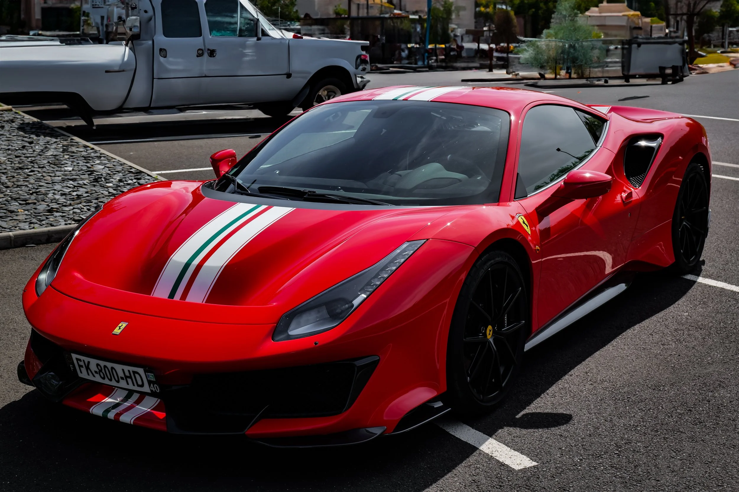 Une voiture rouge Ferrari sportive avec des rayures italiennes blanches, vertes et rouges sur le capot et le toit, stationnée dans un parking.