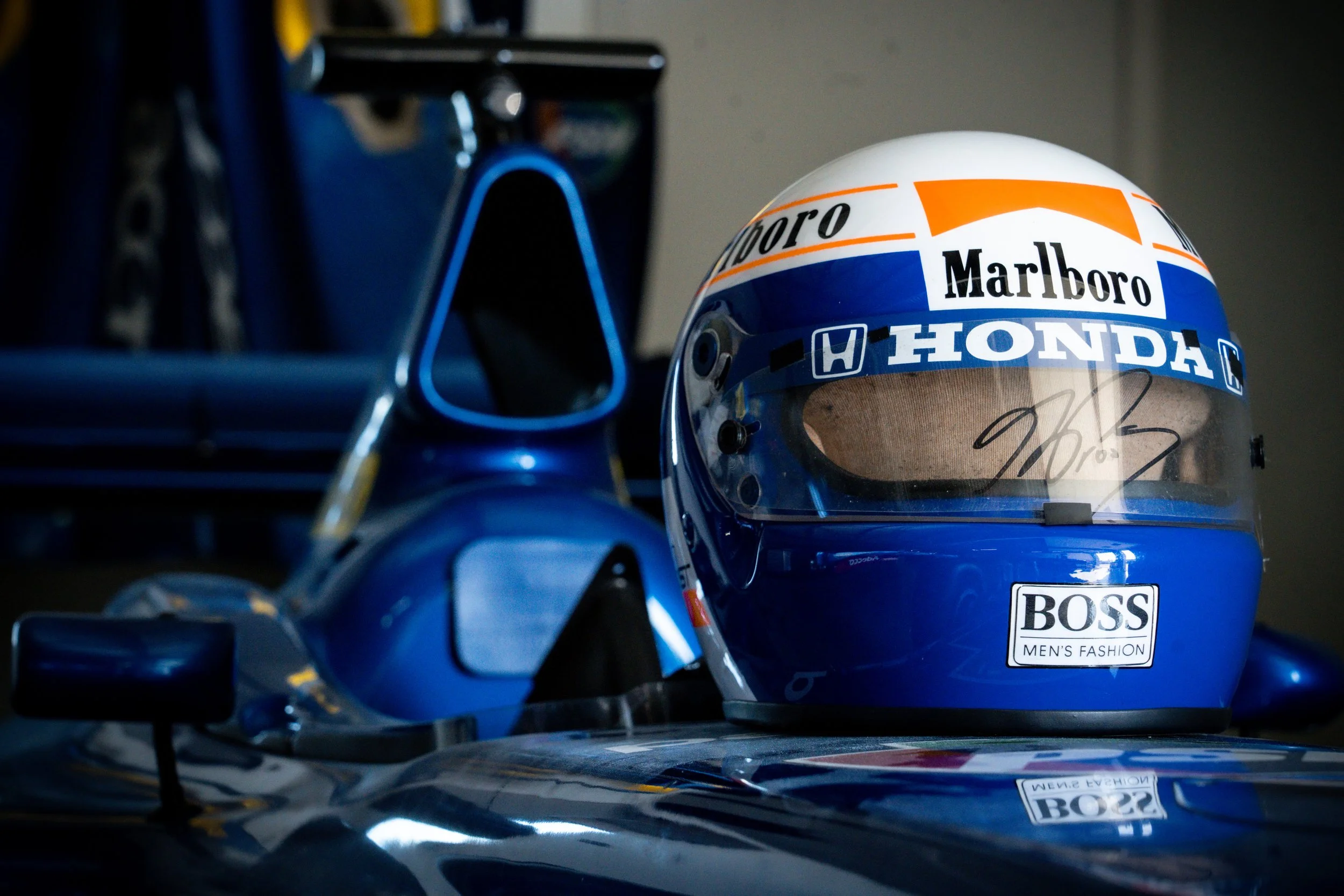Casque de pilote de course avec des sponsorings, posé sur une voiture de course dans un garage.