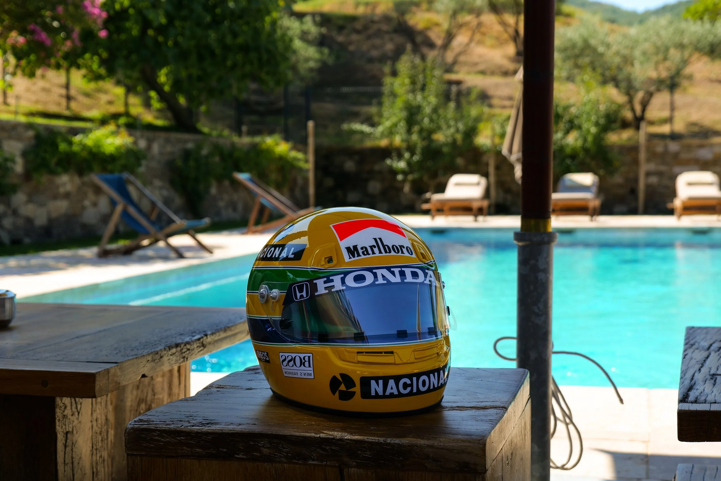 Casque de course de formule 1 sur une table près d'une piscine, avec des chaises longues en arrière-plan.