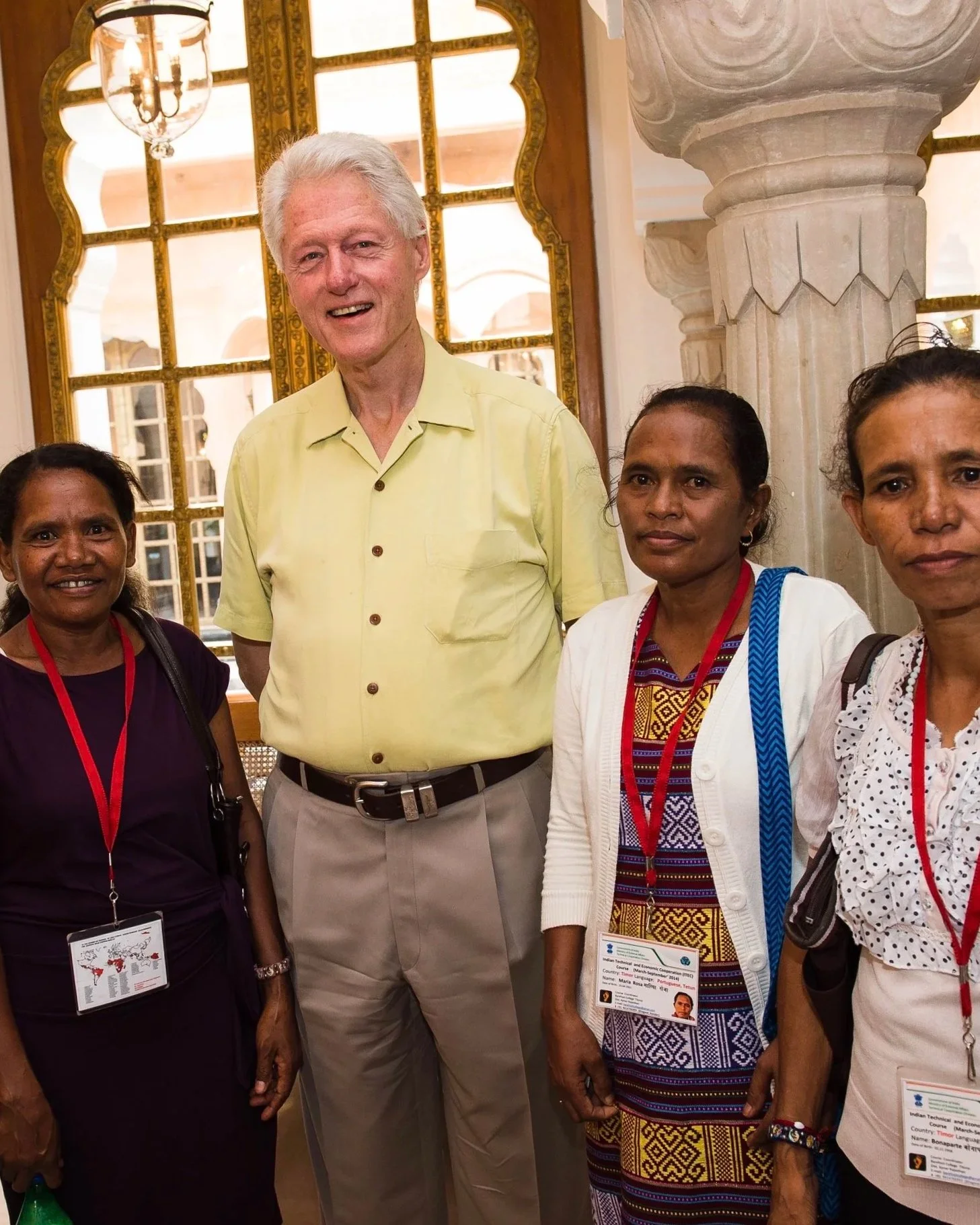 A group photo of Indonesian women and former President Bill Clinton standing inside a building with ornate decor, including large windows and marble columns.