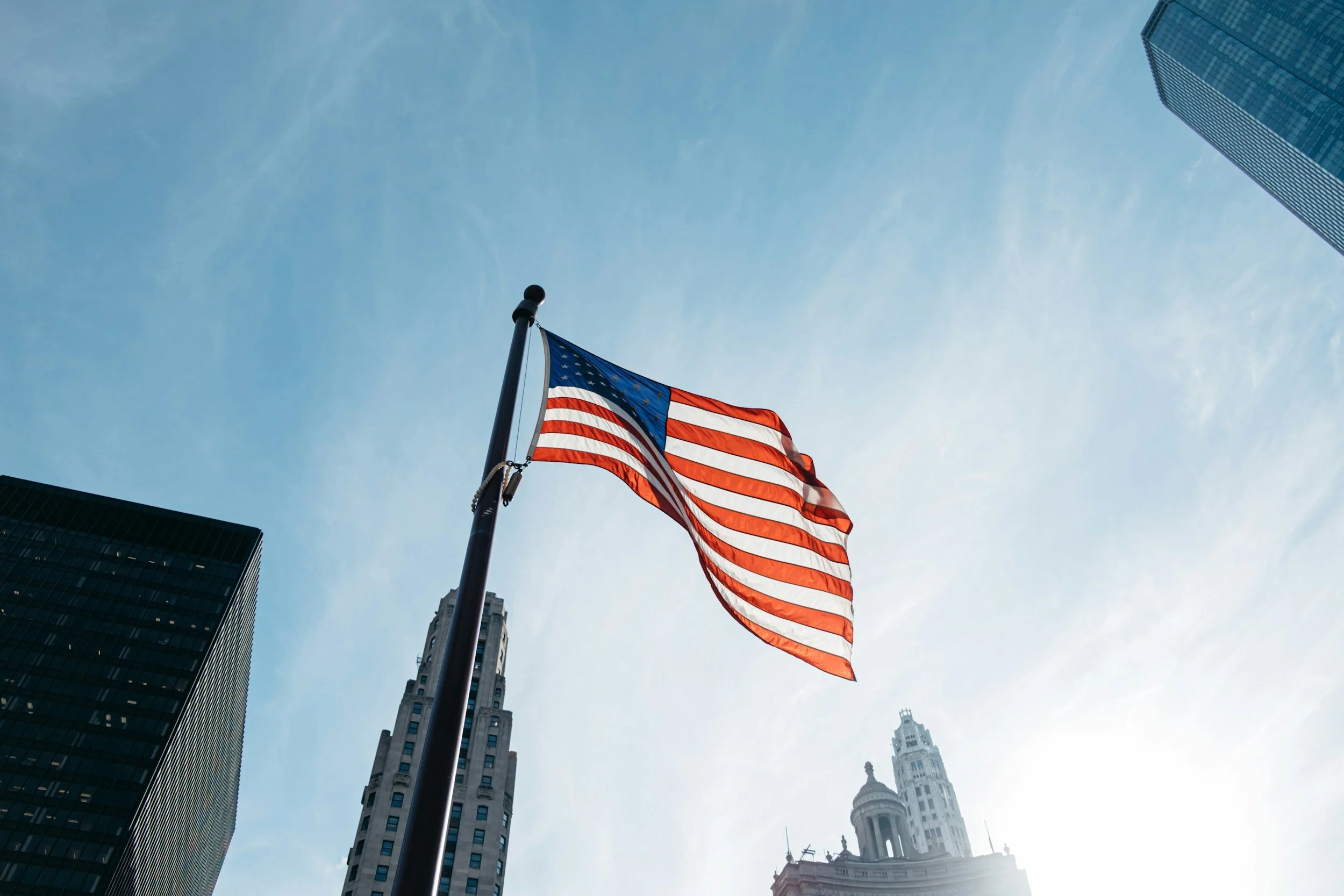 American flag waving in the breeze with tall skyscrapers in the background and the sky overhead.