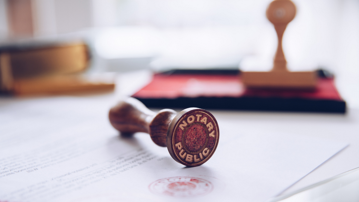 A wooden notary public stamp lying on a document, with other stamps and documents in the blurry background.