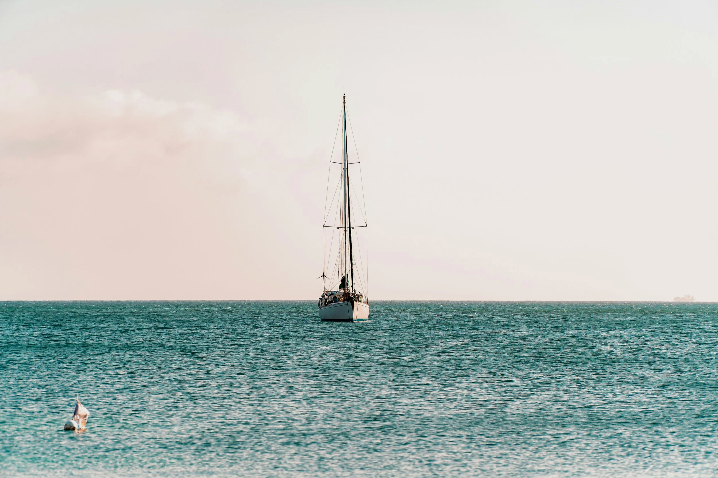 A sailboat on calm ocean waters with a cloudy sky background.