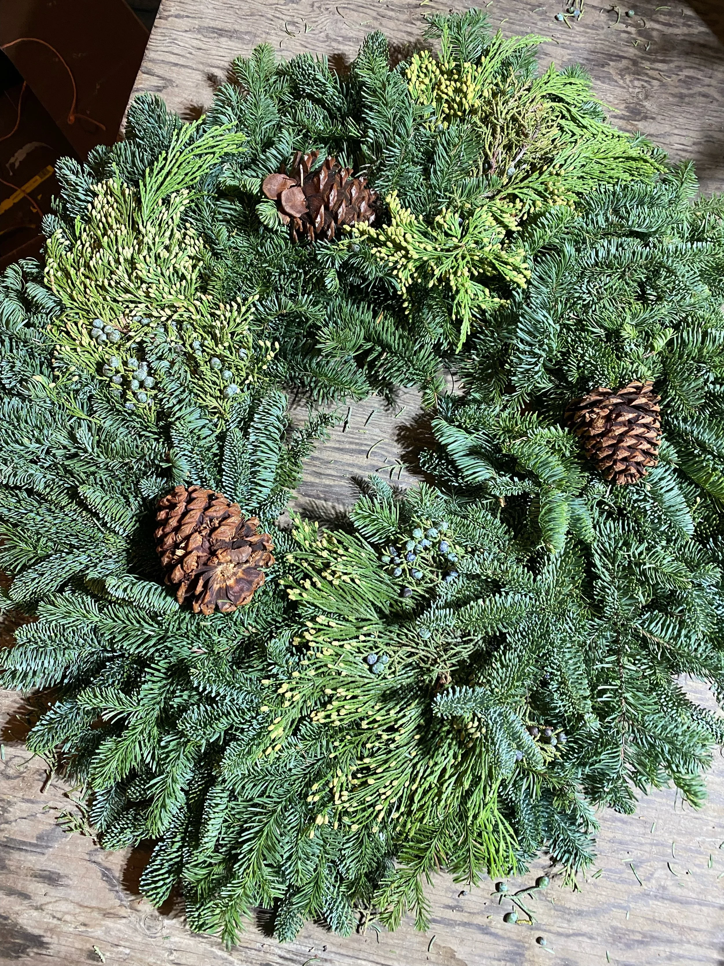A Christmas wreath made of evergreen branches and pinecones on a wooden surface.