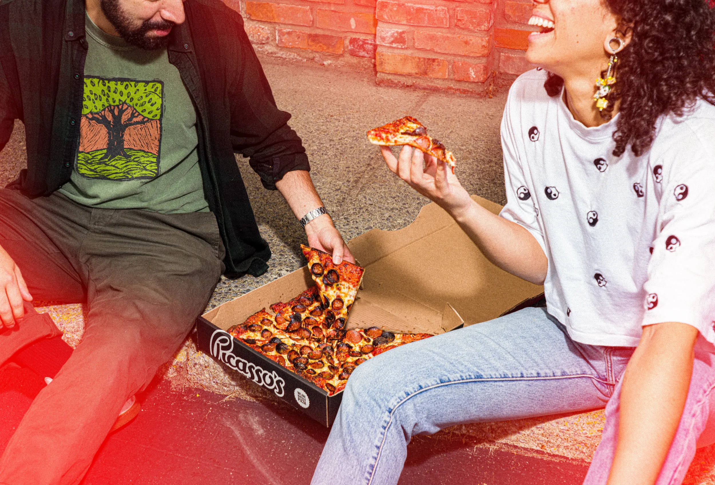 Best friends enjoying a couple of delicious slices of Buffalo style pizza from Picasso's Pizza.