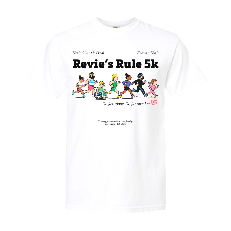 White T-shirt with text and graphics. The shirt mentions Utah Olympic Oval Kearns, Utah, and features cartoon characters running, including a character in a wheelchair. Text reads 'Revie's Rule 5k' and includes a slogan 'Go fast alone. Go far together.' with additional text about giving power back to the family and the date November 1st, 2025.