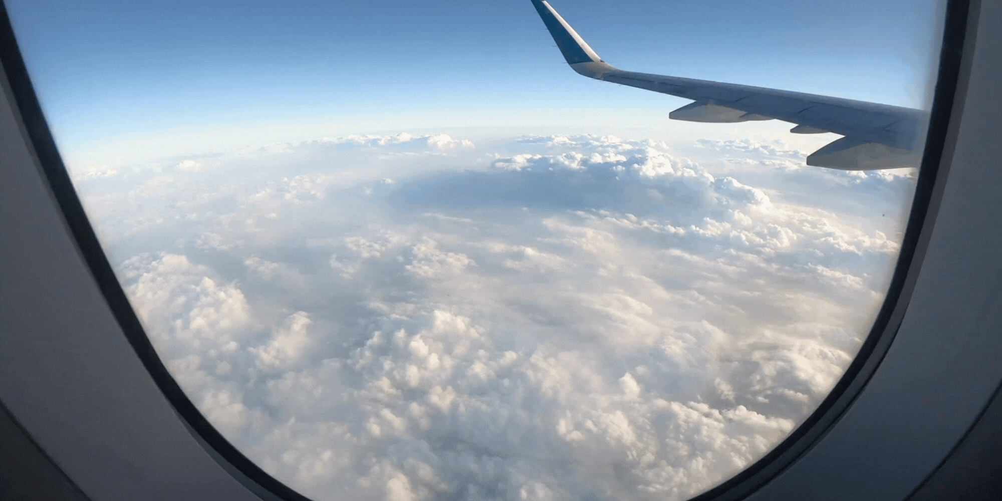 View from an airplane window showing clouds and the wing of the airplane in the sky.