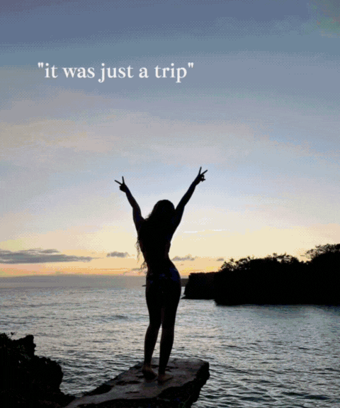 Silhouette of a woman standing on a rock at sunset with arms raised in a V shape and peace signs, overlooking the ocean with an island in the distance, and the quote "it was just a trip" in the top left corner.